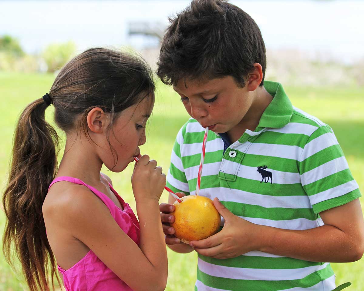 two children enjoy fresh grapefruit juice straight from the fruit with striped straws.