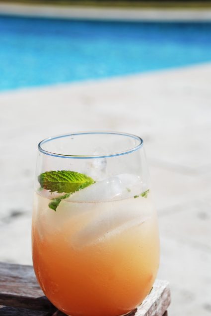 grapefruit mojito with mint leaf in glass sitting outside near the pool