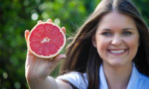Young woman holding half of a SweeterSorts Florida Red Grapefruit