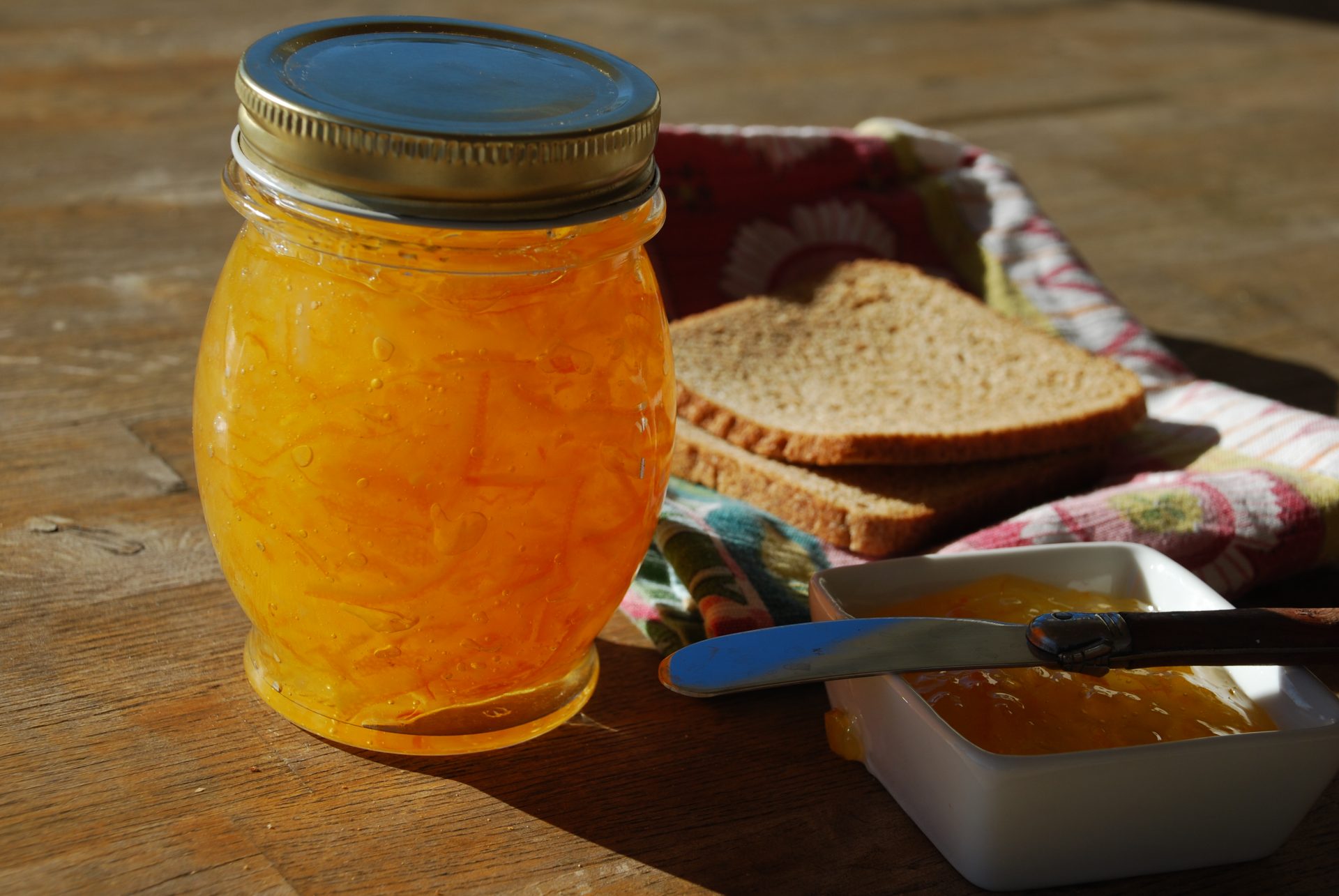 homemade tangerine marmalade in mason jar with toast bread and knife on countertop
