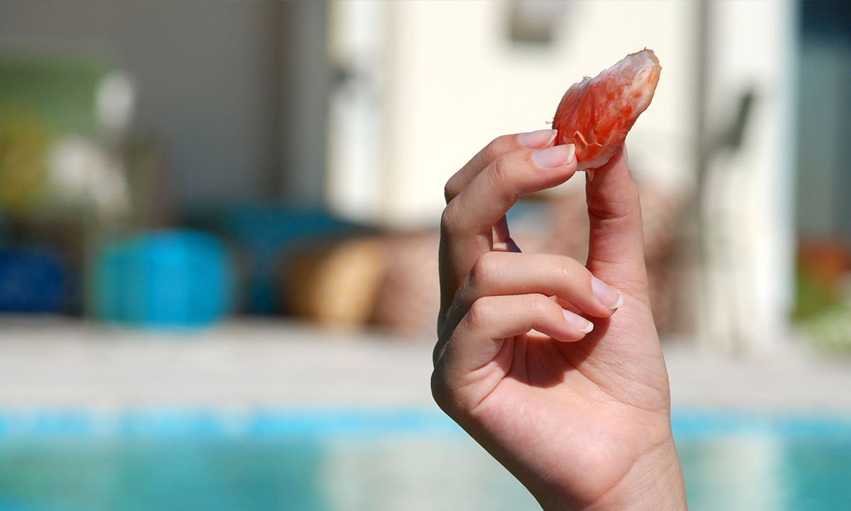 Hand holding SweeterSorts grapefruit wedge while outside by the pool
